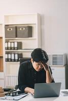 Frustrated Asian young businessman worker working on table in office. Busy employee worker people feel tired and headache from late work and overwork job document on computer desk at company workplace photo