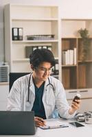 Handsome young doctor with a beard and a lab coat taking of his glasses to read an email in his laptop photo