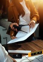 Team of multiethnic architects working on construction plans in meeting room. Engineers discussing on project in office. Mature businessman and woman standing around table working on blueprint. photo
