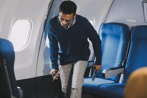 Side view millennial businessman drinking coffee, and using laptop while sitting comfortable seat on airplane cabin photo