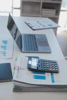 Close up view of simple workspace with laptop, notebooks, coffee cup and tree pot on white table with blurred office room background photo