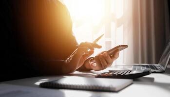 Side view shot of a man's hands using smart phone in interior, rear view of business man hands busy using cell phone at office desk, young male student typing on phone sitting at wooden table, flare photo