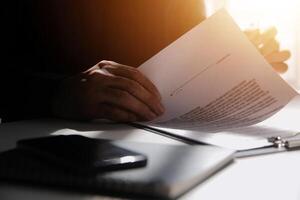 Asian businessman reviewing document reports at office workplace with computer laptop. legal expert, professional lawyer reading and checking financial documents or insurance contract photo