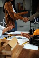 Construction team shake hands greeting start new project plan behind yellow helmet on desk in office center to consults about their building project. in sun light photo