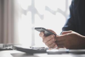 Side view shot of a man's hands using smart phone in interior, rear view of business man hands busy using cell phone at office desk, young male student typing on phone sitting at wooden table, flare photo