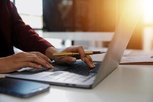 Cropped image of professional businesswoman working at her office via laptop, young female manager using portable computer device while sitting at modern loft, flare light, work process concept photo