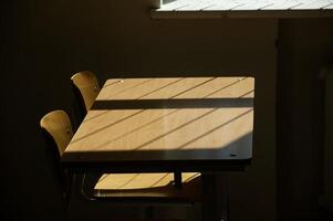 Empty wooden desk and chairs in a quiet and dimly lit classroom with sunlight streaming through the window photo