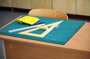Classroom desk equipped with mathematical instruments, ruler, eraser laid out on cutting mat photo