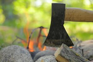 Axe lodged in a log of wood, positioned across from a campfire photo