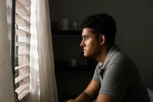 Lonely front facing man looking and thinking in front of a window. concept mental health and masculine crisis. photo