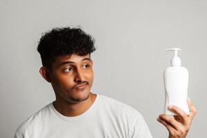 Young man having fun as he practices his skincare routine with a face serum. Man smiling and winking while holding a bottle of a moisturizing beauty product. photo
