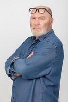 Portrait of an attractive gray-haired man with glasses wearing a denim shirt isolated on a gray background. Bearded grandfather of the European type. photo