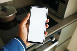 A closeup view of a hand holding a blank mobile phone screen in a modern kitchen photo