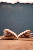 An open book with its pages gently turning rests on a wooden table in the breeze photo