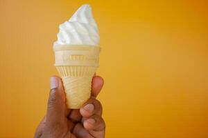 Hand Holding Vanilla Soft Serve Ice Cream Cone against Vibrant Orange Background photo