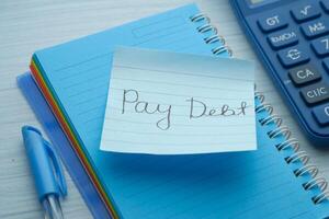 pay debt word on notepad with calculator, close up photo