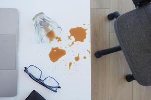 A drink was accidentally spilled on a desk with a laptop and glasses, creating a mess photo