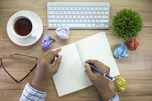 There is a workspace set up with a notebook, keyboard, coffee cup, and crumpled papers on the desk photo