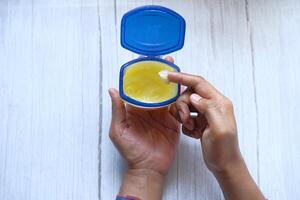 A hand is using petroleum jelly from a blue container for skincare product application photo