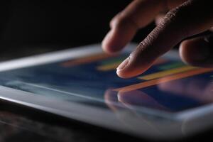 An image showing a hand interacting with a tablet screen displaying business data photo