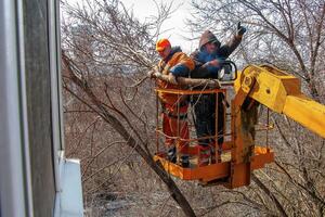 Dnepr, Ukraine - 03.20.2024 Municipal service workers stand with a chainsaw in a crane basket and trim dangerous trees photo