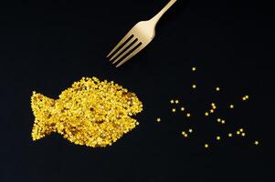 Fish made of golden glitter stars confetti and fork on black background. Creative trendy festive holiday layout. Minimal seafood party concept. Luxury flat lay composition. photo