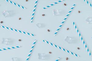 Coffee beans, ice cubes and white and blue paper drinking straws pattern on pastel blue background. Summer drink minimal concept. Flat lay composition. photo