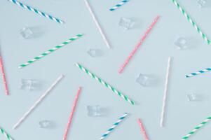 Trendy pattern made with ice cubes and various colorful paper drinking straws on pastel blue background. Summer drink minimal concept. Summertime pastel backdrop. Flat lay composition. photo