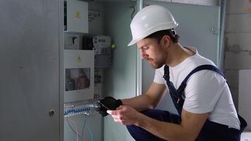 Handsome bearded electrician repairing electrical box. Electrician using screwdriver and a new application on a smartphone video