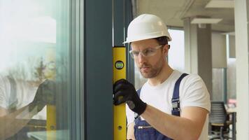 A repairman in uniform installs pvc windows in new office. A man builder measures of the vertical deviation of pvc windows video