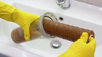 Plumber working in yellow protective gloves holds a dirty water filter in his hands. Dirty rusty filter for water purification. Multi-stage water filter cartridge replacement video