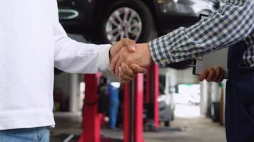 Smiling auto mechanic and indian client shaking hands in service, close up video