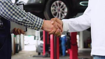 Smiling auto mechanic and indian client shaking hands in service, close up video