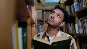 University Library. Talented Indian Boy Standing Next to Bookshelf Reads Book for His Class Assignment and Exam Preparations video