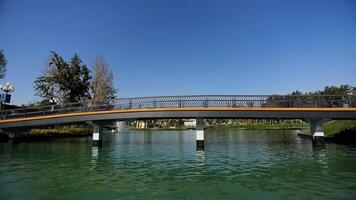 A drone on the water of a city lake in a park surrounded by trees. View of the promenade bridge. Cloudless summer day video
