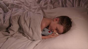 small child boy sleeps restlessly hugging a teddy bear toy at night on bed. The kid son has nightmares video