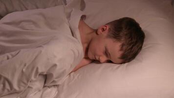 small child boy tosses restlessly in sleep on a pillow under a blanket at night. Sleeping preschooler kid son on bed in bedroom in the evening video