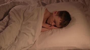 cute kid boy is sleeping happily on a pillow under a blanket in the evening. Child baby son in a dream on bed in the bedroom in the night video