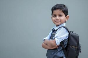 Back to school. A happy boy kid in school uniform, standing with hands crossed folded against isolated gray background. school kid photo