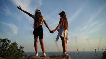 mom and daughter are standing on a rock overlooking the ocean. They are holding hands and smiling. Scene is happy and carefree. video