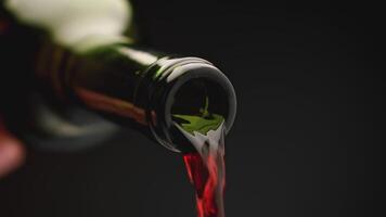 Red wine pours from the neck of bottle. Slow-motion pouring of red wine from a bottle, on a black background. video
