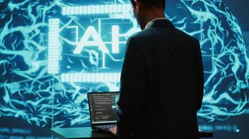 AI system administrator using laptop device in high tech futuristic workspace. Man working on notebook to automatize tasks using artificial intelligence technology, camera A video