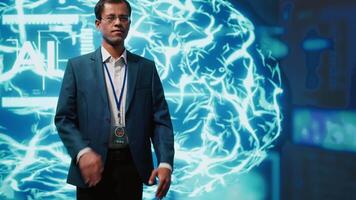 Upbeat engineer in startup doing advancements in AI field. Portrait of happy man standing with arms crossed in front of cutting edge display featuring AI and neural network graphics, camera A video