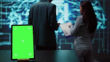 Green screen tablet used by computer scientists in startup doing advancements in AI field. Employees working on mockup device in workspace featuring artificial intelligence systems, camera B video