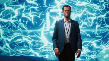 Smiling technician in startup stands with arms crossed, exuding professionalism and expertise. Portrait of cheerful Indian IT expert working in futuristic artificial intelligence workspace, camera A video