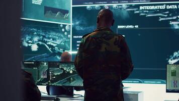 Commander and his crew operating radar systems via CCTV and satellite to detect and track enemy aircraft or missiles. Military officer uses big screen in control center to guarantee safety. Camera A. video
