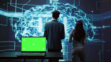 Teamworking AI technicians using green screen laptop for business data analysis. Team of IT experts works on mockup notebook to automatize tasks using artificial intelligence, camera B video