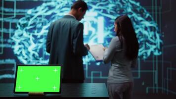 AI programmers colleagues using green screen laptop for business data analysis. IT experts in high tech location work on chroma key notebook to automatize tasks using artificial intelligence, camera B video