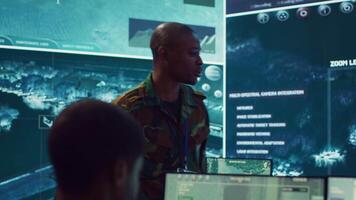Platoon captain handling surveillance and safety operations with crew, dashboard to oversee field missions within enemy territory. Soldiers monitor CCTV satellite footage on big screen. Camera A. video
