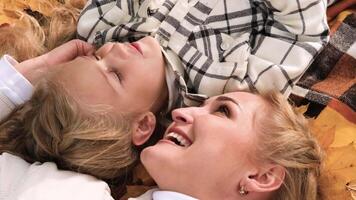 The family has fun in the park. Girl and mother lie on a blanket and look at autumn leaves video